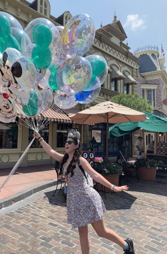 Hannah Vaughn at Disney theme park, holding colorful Disney character balloons, joyful experience, vibrant atmosphere, family-friendly vacation, memorable day at Disney's Magic Kingdom.